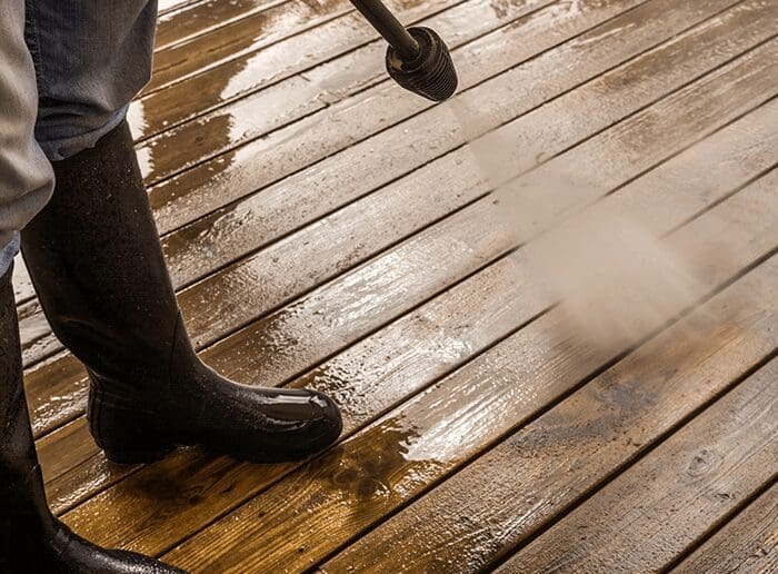 A person using a power washer on a wooden deck.